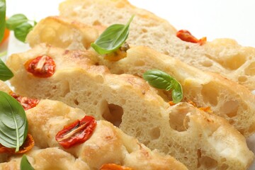 Cut delicious focaccia with tomatoes and basil on table, closeup