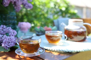 Beautiful lilac flowers and tea on wooden table in garden, closeup