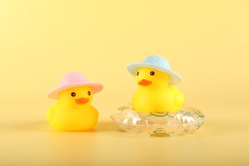 Cute rubber ducks in hats and inflatable ring on yellow background
