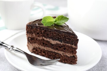 Piece of delicious chocolate cake with mint and fork on table, closeup