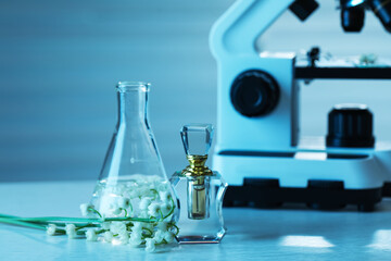 Making luxury perfume. Essential oils in glassware, flowers and microscope on white wooden table, closeup