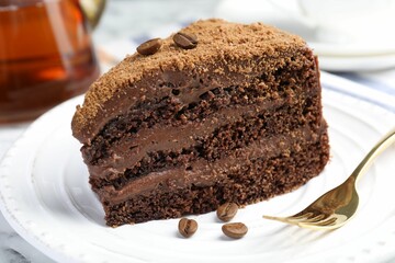 Piece of delicious chocolate cake with coffee beans and fork on white table, closeup