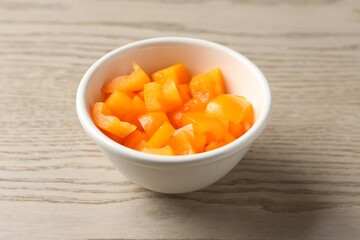 Pieces of fresh orange bell pepper in bowl on wooden table, closeup