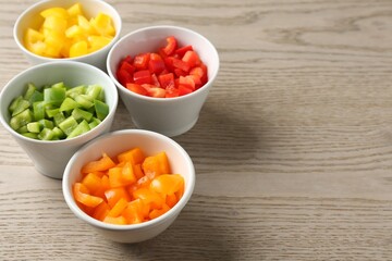 Pieces of fresh colorful bell peppers in bowls on wooden table, closeup. Space for text