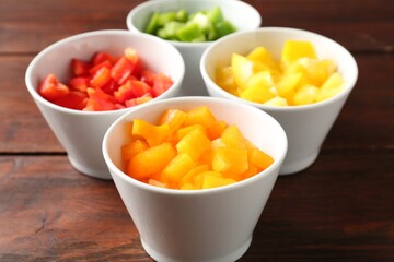 Pieces of fresh colorful bell peppers in bowls on wooden table, closeup