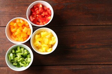 Pieces of fresh colorful bell peppers in bowls on wooden table, flat lay. Space for text