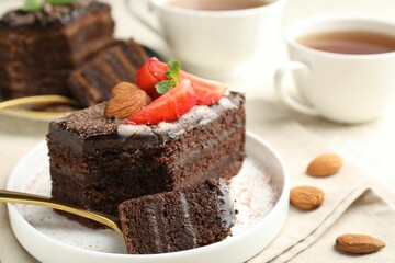 Piece of delicious chocolate cake with strawberry, almonds and tea on table, closeup