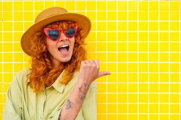 Enthusiastic redhead influencer pointing aside on yellow tiled wall