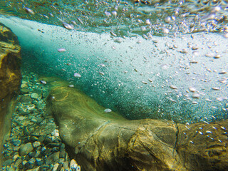 The underwater world of a cold Norwegian river: crystal clear water, stones at the bottom, and playing air bubbles in the stream.