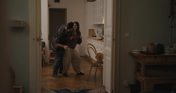 Side view Cheerful guy and girl in pajamas dancing impromptu dance during romantic evening in cozy apartment at home. Guy and a girl improvise and dance at home