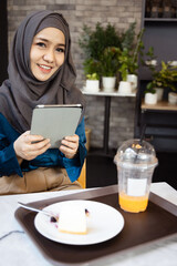 Asian female Muslim Digital Nomad Worker working remotely in cafe, happy smiling positive mood and facial expression