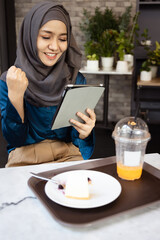 Successful Asian female Muslim Digital Nomad Worker working remotely in cafe, happy smiling exciting mood and facial expression