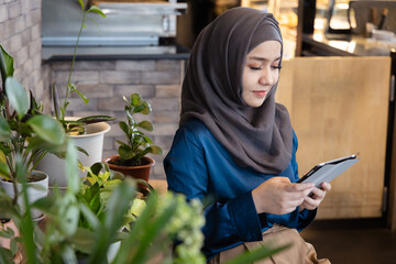 Asian female Muslim Digital Nomad Worker working remotely in cafe, relaxed and carefree mood and facial expression