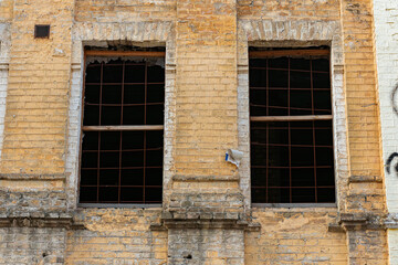 Two barred windows in a yellow brick wall of an abandoned building, paint peeling.
