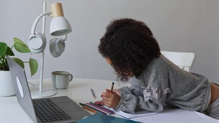 Primary school African American Student child with headphones hand writing in book using laptop. Distance learning online education. School girl studying at home with digital tablet computer and doing - Powered by Adobe
