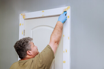 Homeowner works applies wood filler on door trim, using tool while preparing before painting