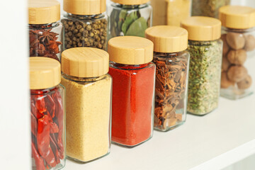 Many different aromatic spices in jars on white shelf indoors, closeup
