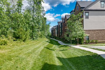 sidewalk along rows of modern brick townhouses with landscaping and a large lawn.