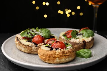 Tasty stuffed mushrooms served on black table against blurred background, closeup. Bokeh effect