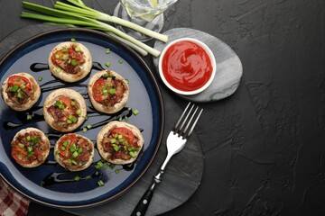 Tasty stuffed mushrooms served on black table, flat lay