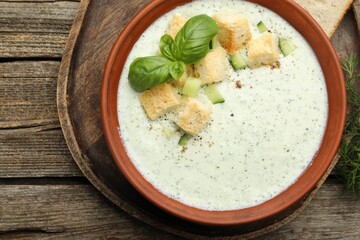 Tasty cucumber soup with croutons and basil on wooden table, top view