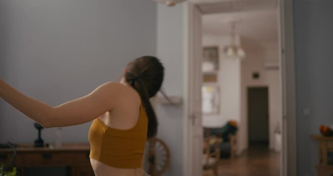 Dynamic scene cheerful girl in yellow top dancing and improvising modern dance in cozy apartment. Dance of a cheerful girl at home