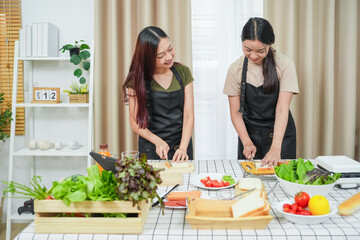 Two asian woman study online in the classroom making sandwich together in the home kitchen. Homemade and Learn online concept