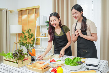 Two asian woman study online in the classroom making sandwich together in the home kitchen. Homemade and Learn online concept