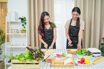 Two asian woman study online in the classroom making sandwich together in the home kitchen. Homemade and Learn online concept