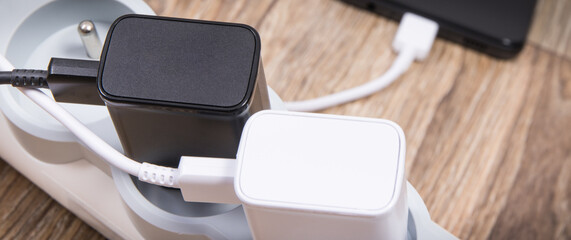 Black smartphone and chargers connected to electrical power strip. Various devices charging concept