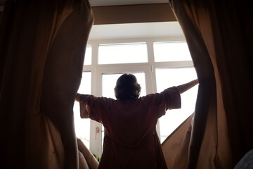 girl woman opens curtains in bedroom in morning. sunlight shines through window. start of a new day