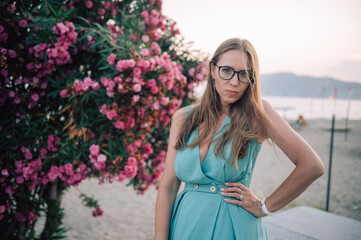 A graceful woman in a turquoise dress poses near blooming pink flowers, enjoying a peaceful moment...