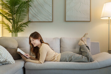 Obraz premium Carefree young woman lying on a couch and enjoying her book.