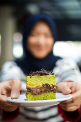 A slice of green tea cake with chocolate filling, sprinkled with grated chocolate, on a small white plate served by hand