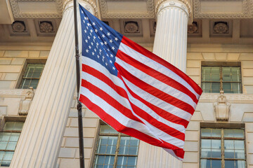 Patriotic American flag flutters in breeze near architectural columns of historic government structure at Washington DC