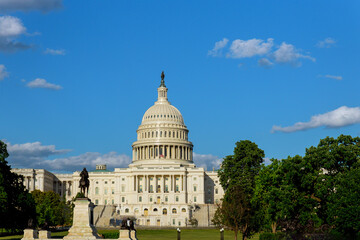 Fototapeta premium U.S. Capitol Building shines under blue sky, fluffy clouds, lush green trees.