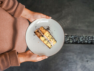 Hands holding a white plate with a tempting piece of layered cake, with chocolate crumbs and cream filling. A delicious dessert