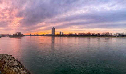 Obraz premium Sunset panoramic view of a calm river with distant city buildings