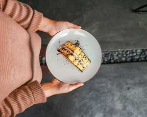 Hands holding a white plate with a tempting piece of layered cake, with chocolate crumbs and cream filling. A delicious dessert