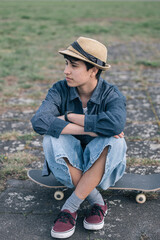 Young skater girl sitting on skateboard looking away wearing casual clothes