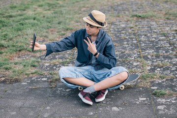Teenager girl taking selfie while sitting on skateboard and making peace sign