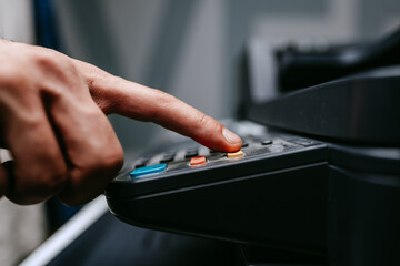 Person pressing buttons on office equipment in a busy workspace during the day