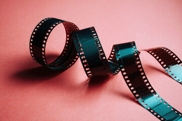 Coiled film strip lies artistically on pink background, showcasing studio shot with artistic angle. image evokes sense of nostalgia and creativity