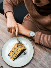 A person cuts into a delicious slice of layered cake with chocolate crumbs and creamy filling, served on a white plate on a wooden table