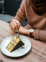 A person cuts into a delicious slice of layered cake with chocolate crumbs and creamy filling, served on a white plate on a wooden table