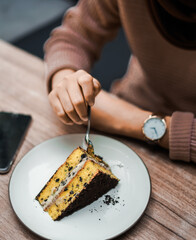 A person cuts into a delicious slice of layered cake with chocolate crumbs and creamy filling, served on a white plate on a wooden table
