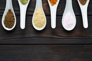 Different superfood powders in spoons on wooden table, flat lay. Space for text