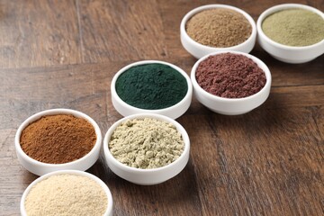 Different superfood powders in bowls on wooden table, closeup