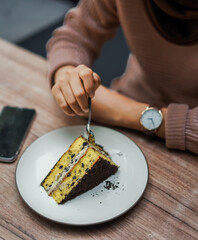 A person cuts into a delicious slice of layered cake with chocolate crumbs and creamy filling, served on a white plate on a wooden table