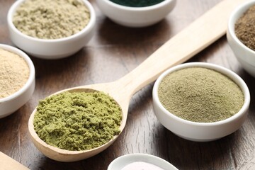 Different superfood powders in bowls and spoons on wooden table, closeup